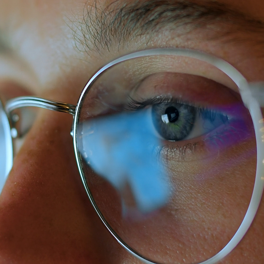 Image of a face wearing glasses reflecting an image on a computer screen