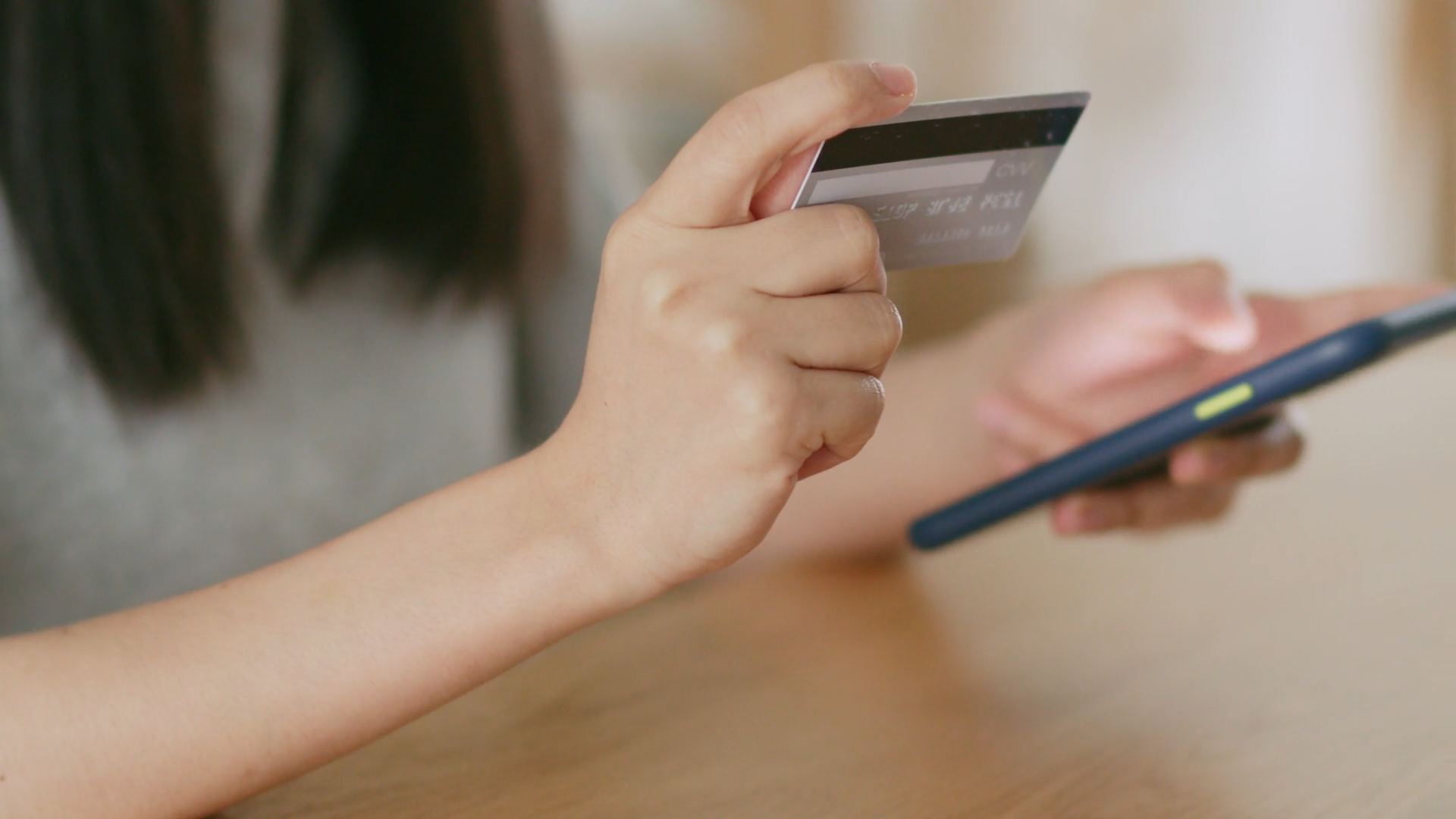 A woman making a payment using a card and a cell phone.