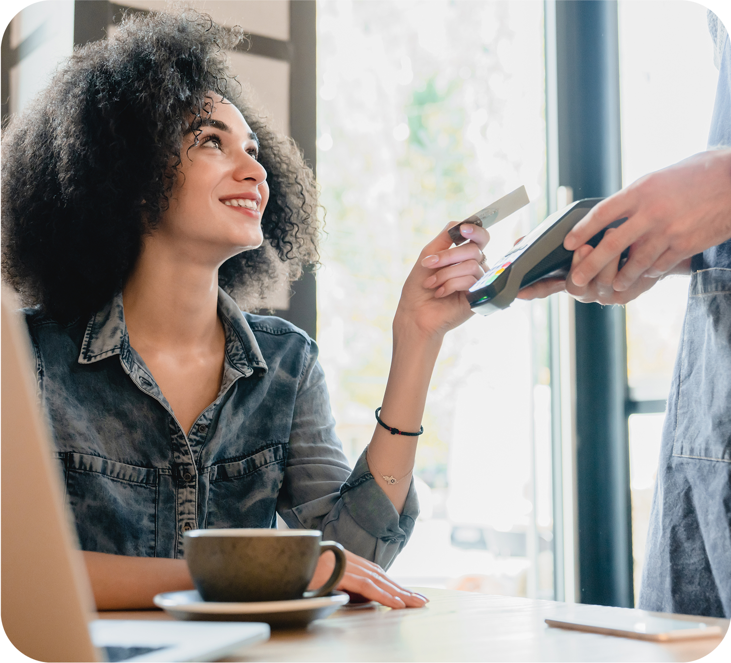 A woman making a payment at a coffee shop using a card and a cell phone.